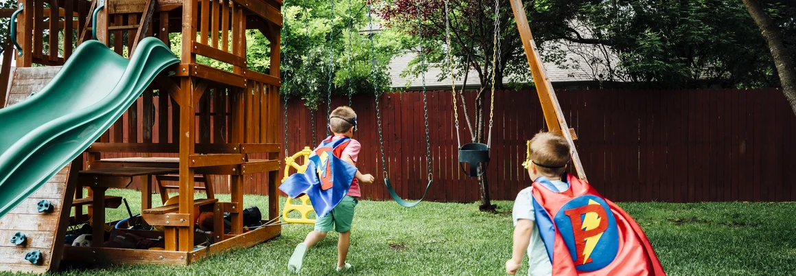 Zwei Kinder mit Umhängen rennen im Garten.